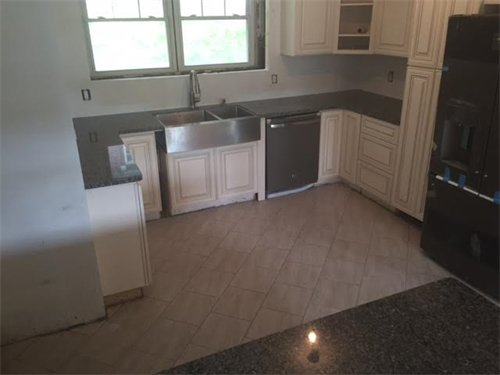 Kitchen with white cabinets, stainless steel sink, dark countertops, and light-colored tiled floor.