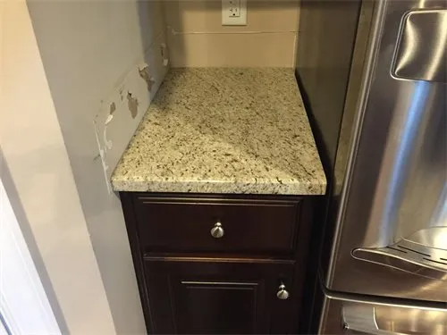 Dark wood cabinet with granite countertop between wall and stainless steel refrigerator.