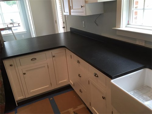 Black countertop on white cabinets in a kitchen with a window and a farmhouse sink.