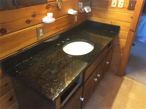 Bathroom vanity with black countertop, wooden cabinet, and white sink. Wooden walls and floor.