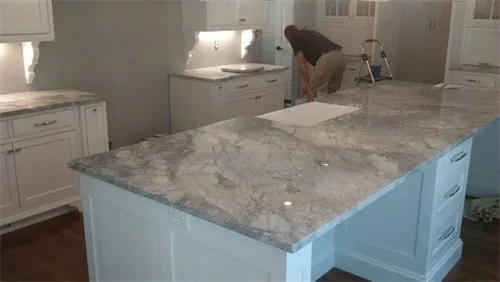 Kitchen with white cabinets, granite countertops, and a worker installing them.