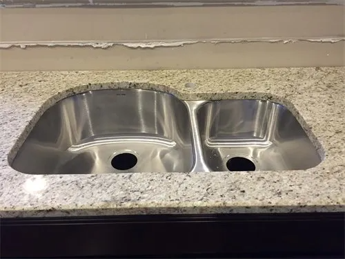 Stainless steel double kitchen sink set in speckled granite countertop.