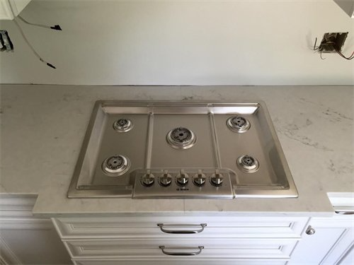 Stainless steel gas cooktop built into a light gray countertop above white cabinets.