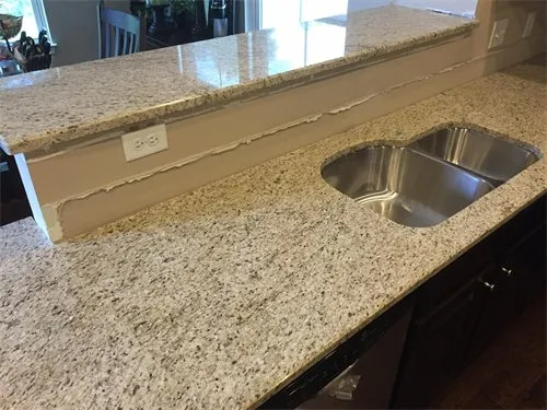 Granite countertop with built-in stainless steel sink, beige backsplash, and power outlet.