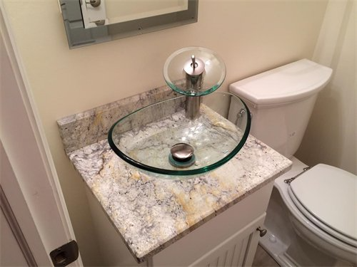 Glass sink on a granite countertop, with a toilet and mirror in a bathroom.