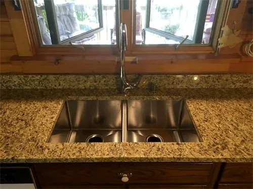 Stainless steel double sink in a granite countertop, under a window.