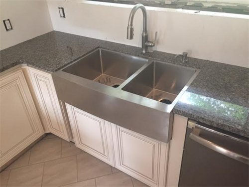Stainless steel farmhouse kitchen sink installed in a remodeled kitchen with granite countertops.