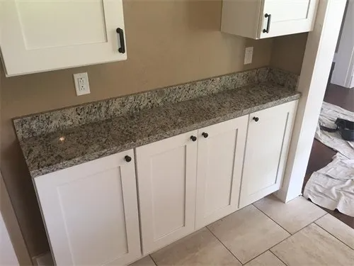 White cabinets with a granite countertop in a room with beige walls and tile flooring.