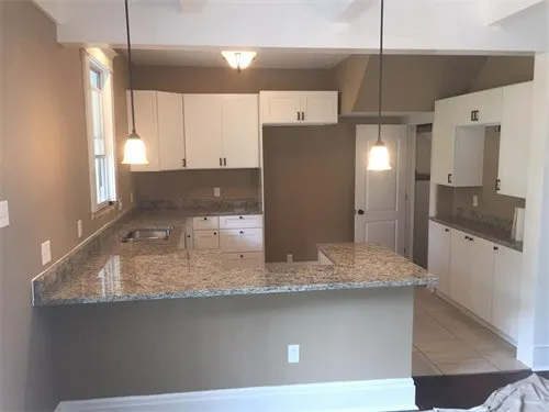 Newly renovated kitchen with white cabinets, granite countertops, and pendant lights.