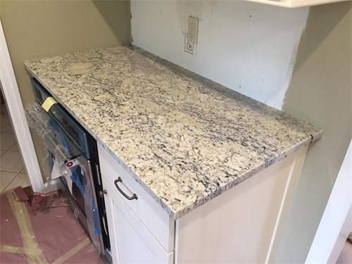 Granite countertop on white cabinet with oven, unfinished wall above, and red flooring.