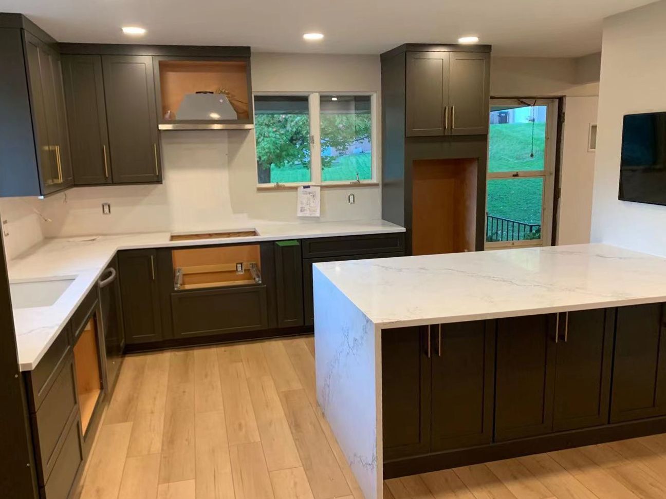 Newly renovated kitchen with dark green cabinets, white countertops, and light wood flooring.