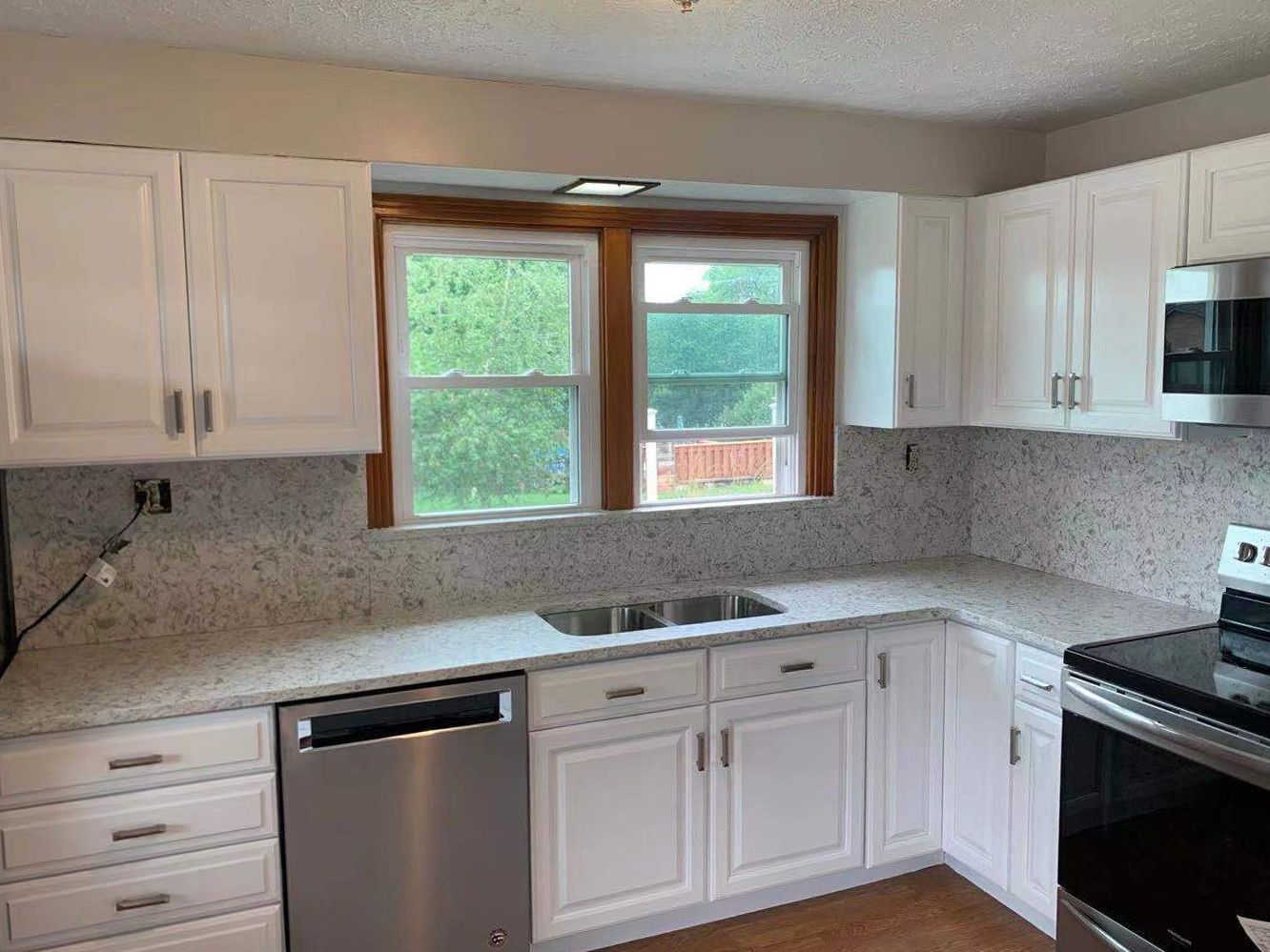 White kitchen with granite countertops, white cabinets, and stainless steel appliances. Windows with a view.
