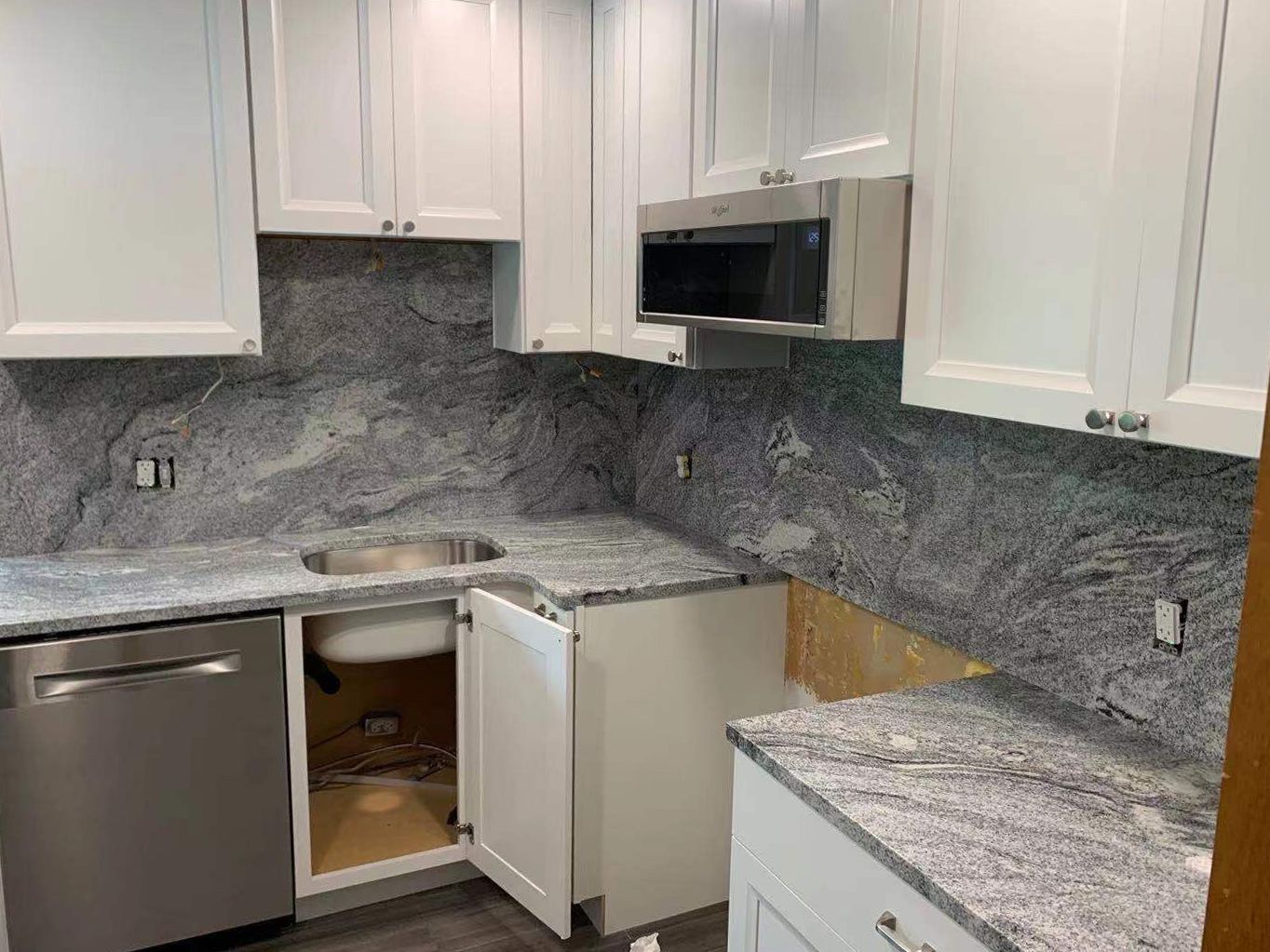 White kitchen cabinets with grey granite countertops and backsplash. Dishwasher, sink, and microwave visible.