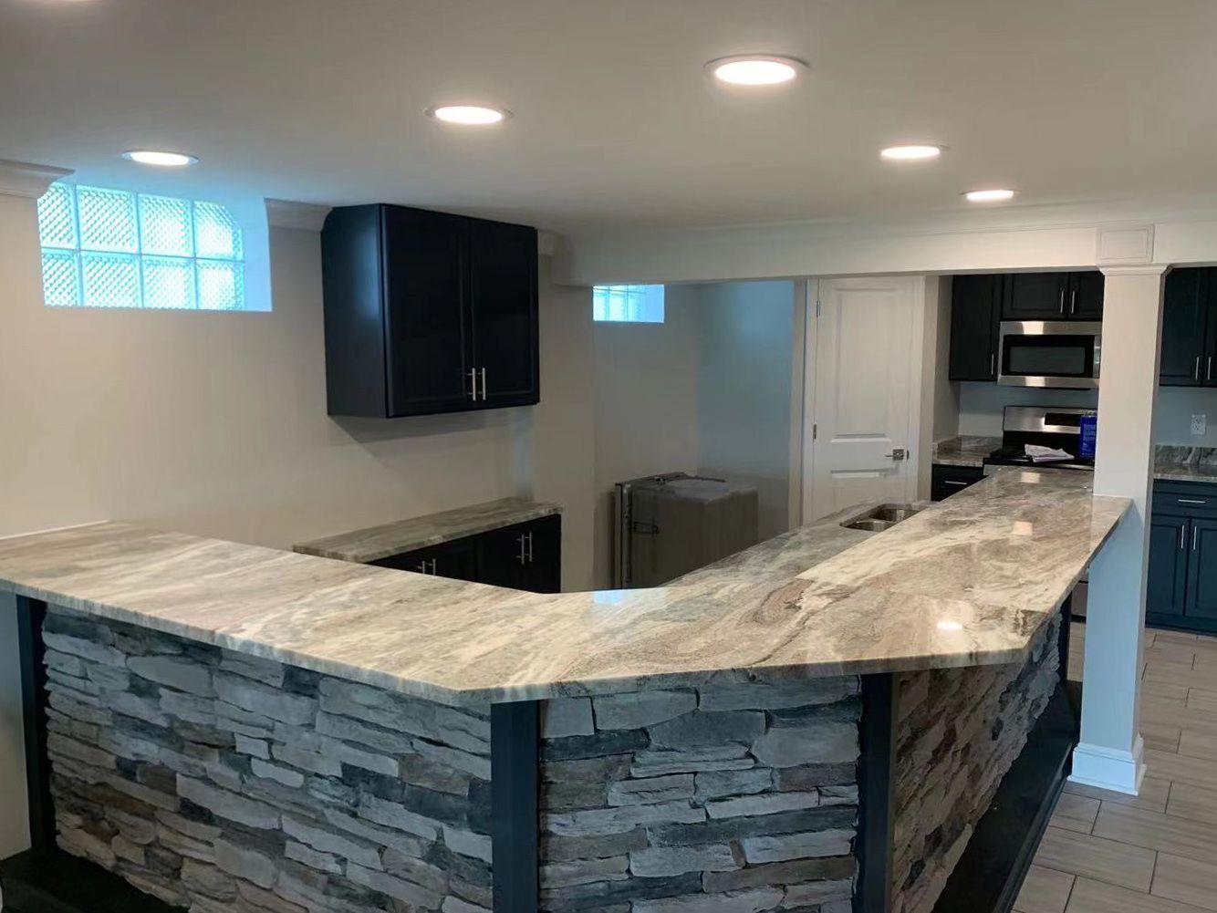 Finished basement with a stone-faced bar, granite countertop, cabinets, and kitchen appliances.