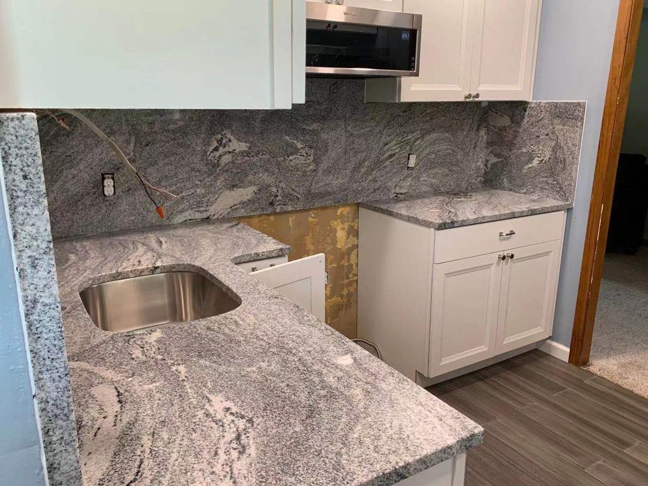 Kitchen with gray granite countertops, white cabinets, stainless steel sink and backsplash.