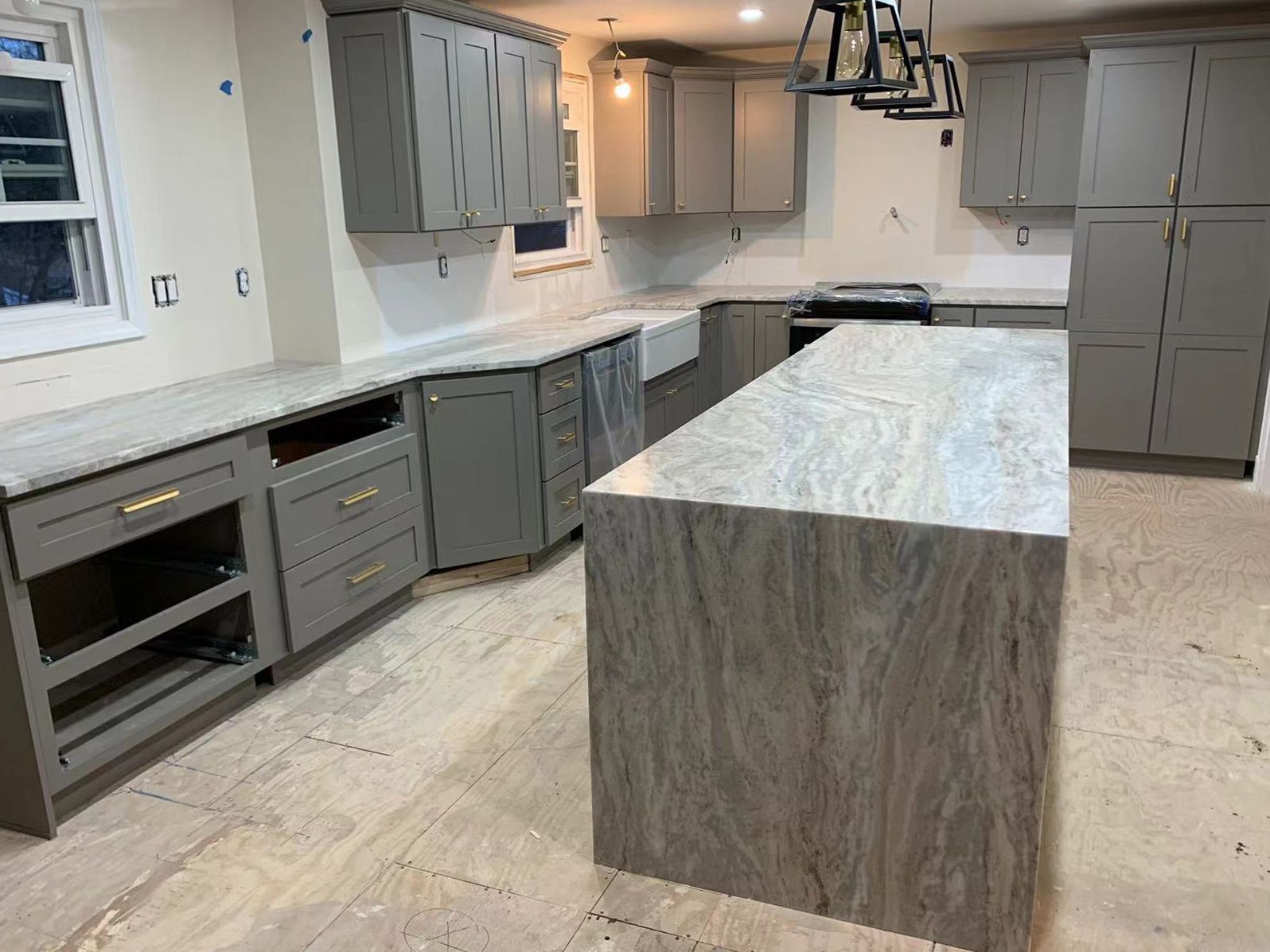 Gray kitchen cabinets with marble countertops and island; under construction.