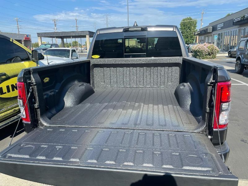 The back of a truck with the bed open is parked in a parking lot.