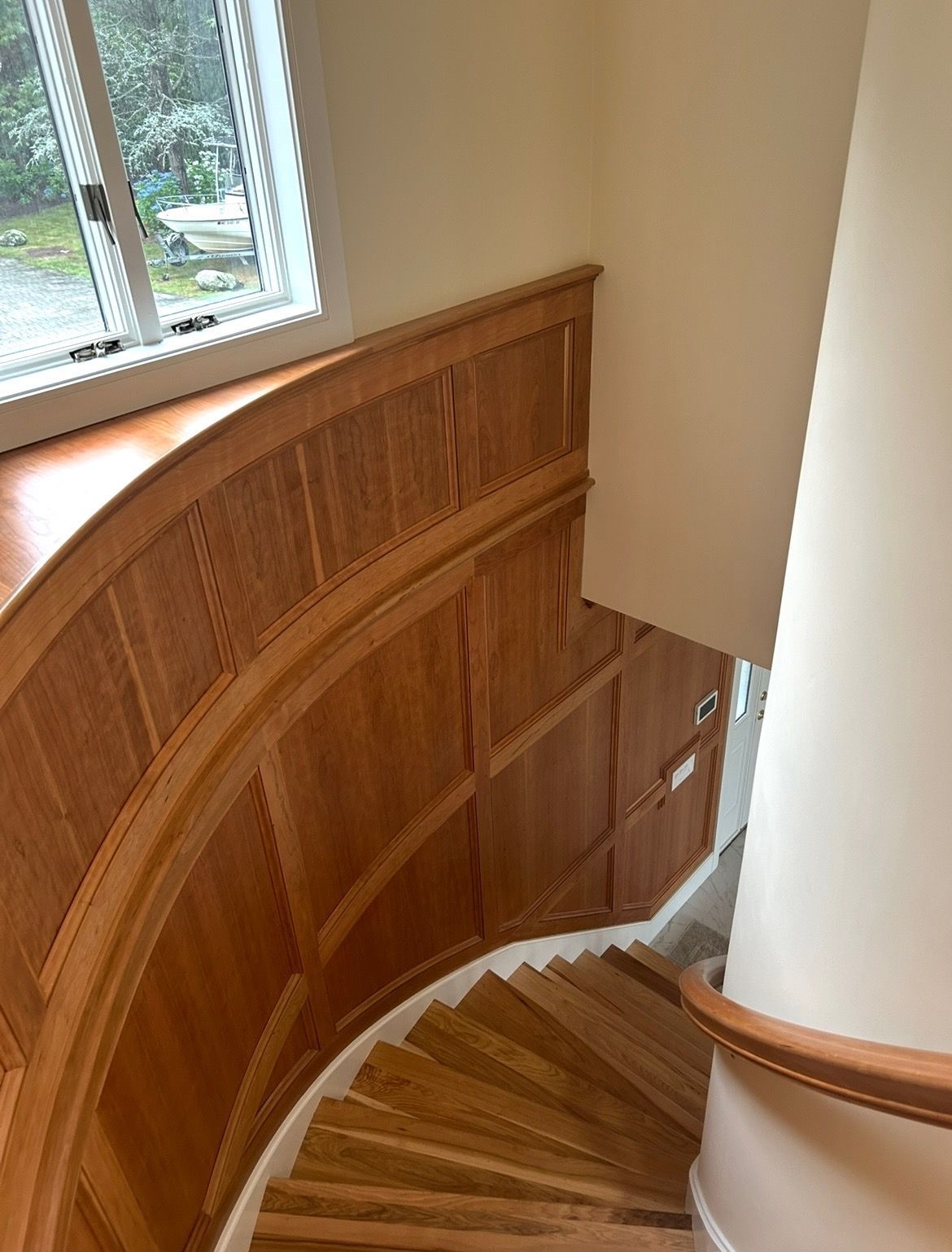 A curved wooden staircase with a white railing and a window.