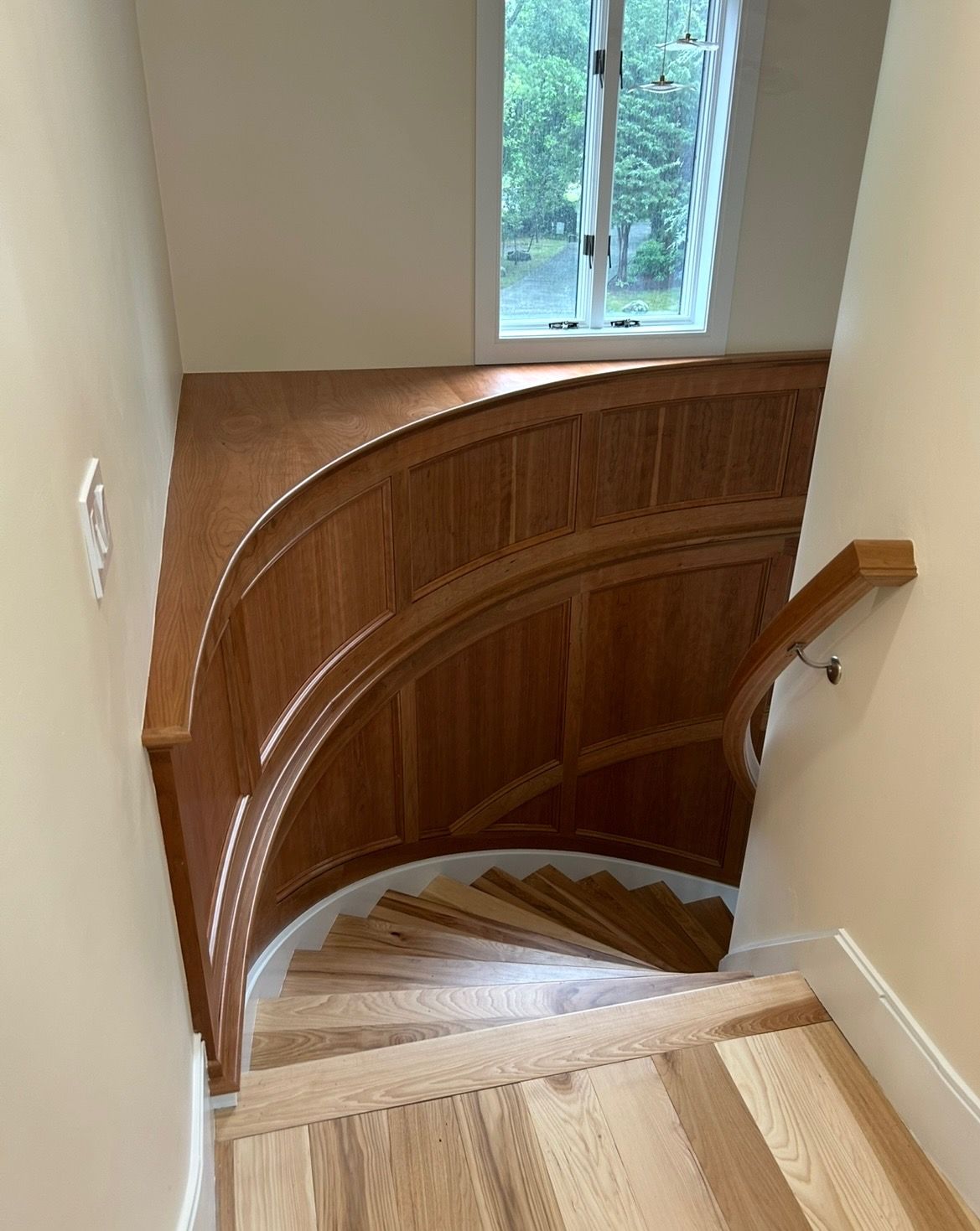 A wooden staircase with a curved railing and a window.