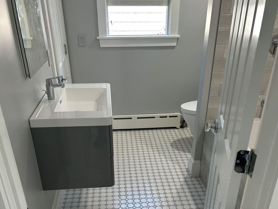 A bathroom with a sink , toilet , mirror and window.