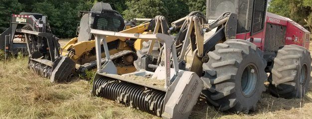 Heavy forestry equipment in a grassy field, including a red harvester and tracked machinery.