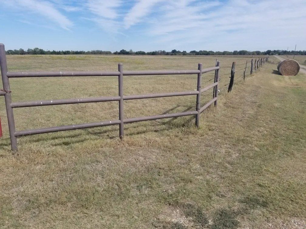 Brown metal fence in a grassy field with a hay bale and a blue sky in the background.