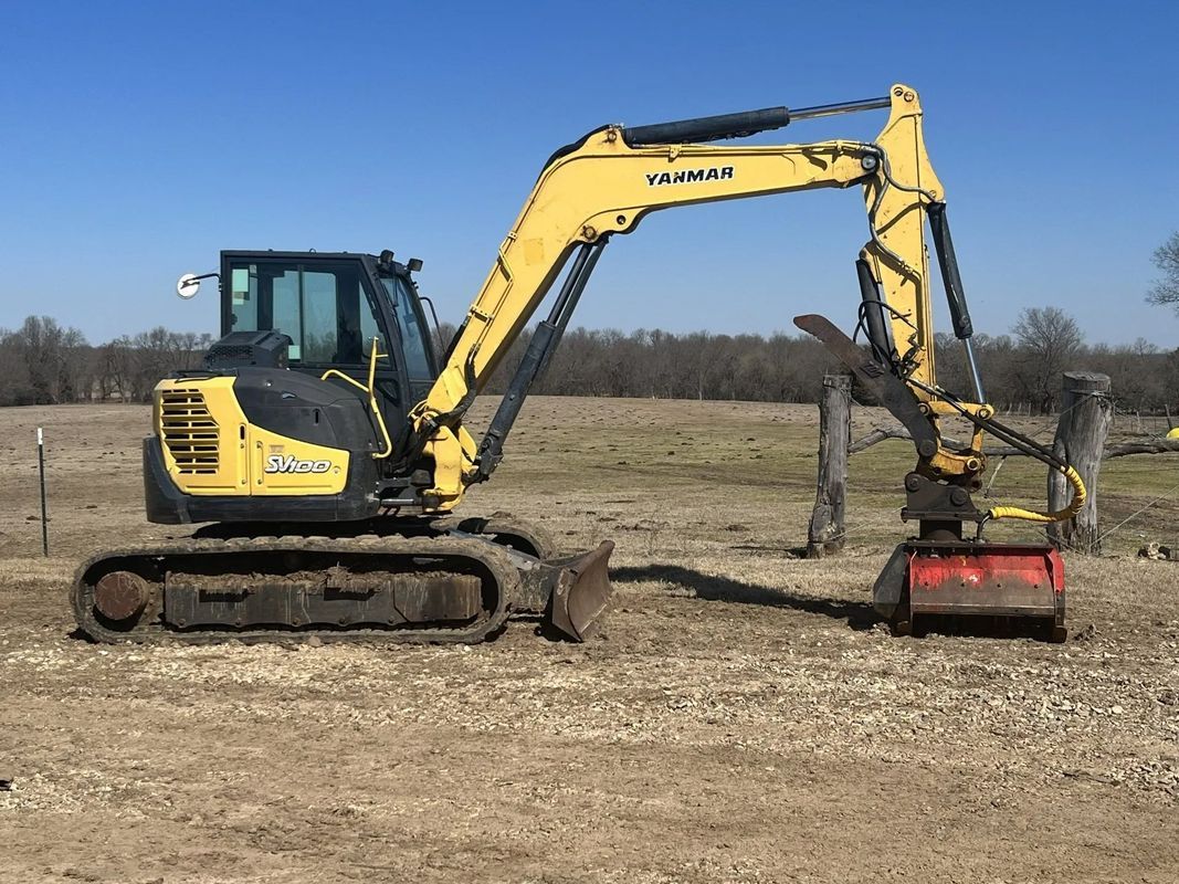 Yellow and black mini excavator with brush cutter attachment in field.