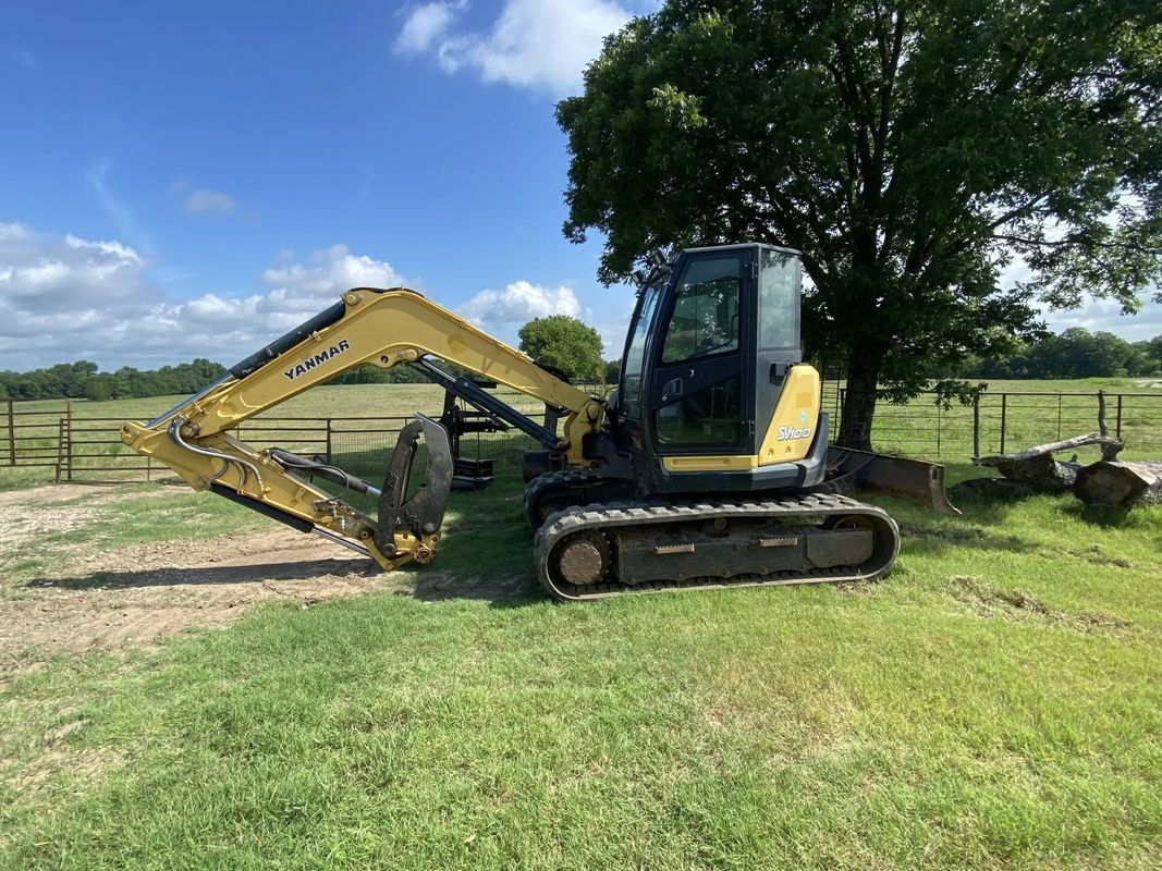 Yellow trackhoe on grass with a raised arm, in a field, under a blue sky.