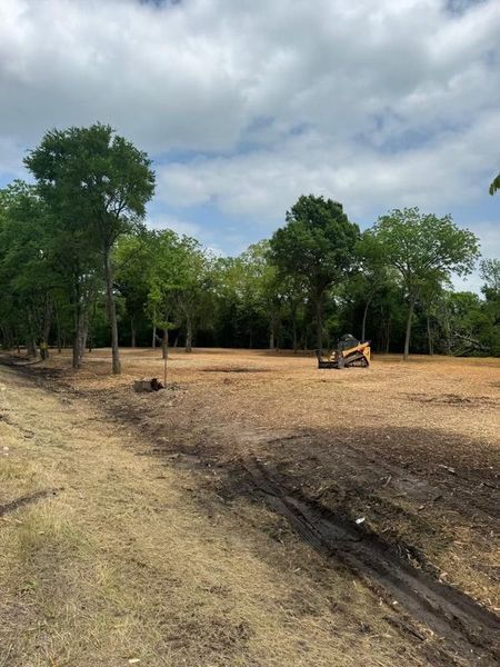 A cleared lot with a small bulldozer, trees in background, cloudy sky.