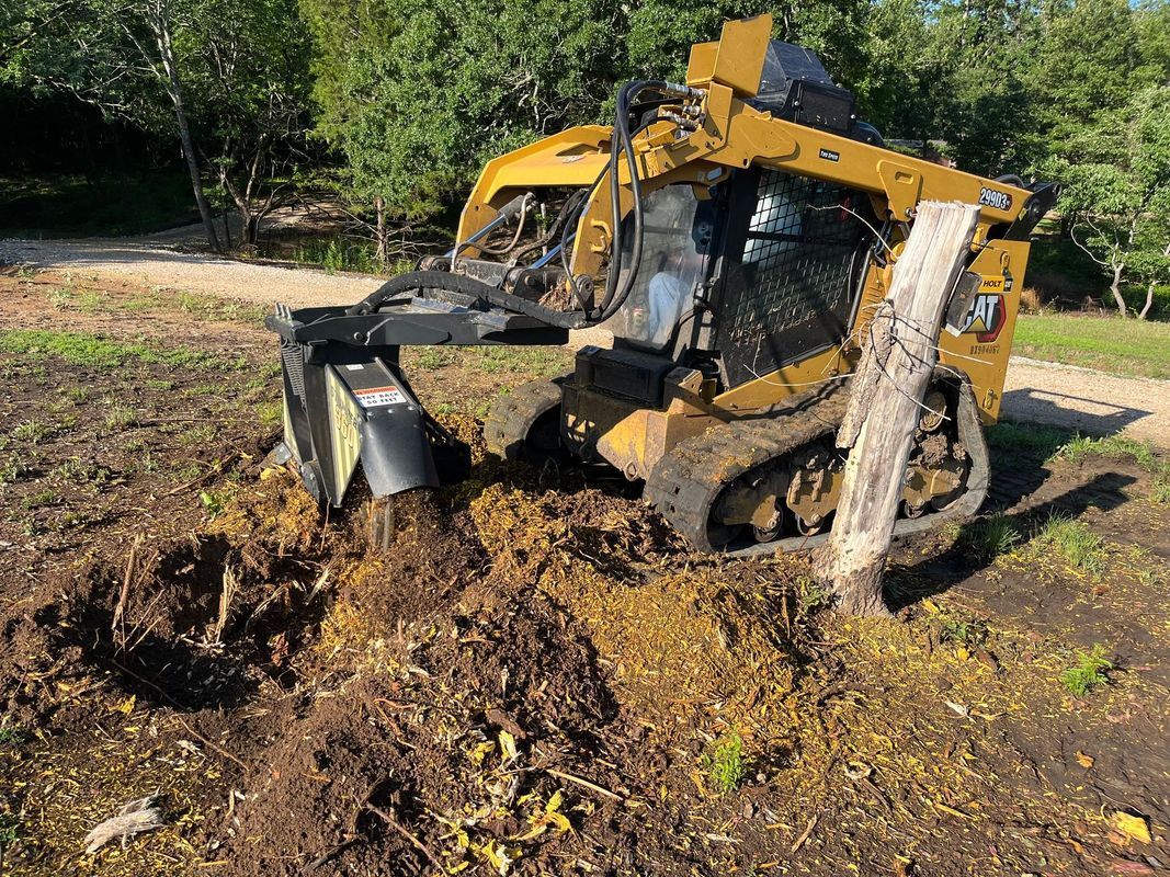 Yellow skid steer with a forestry cutter removing a tree stump.
