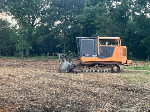 Orange bulldozer on tracks in a field, clearing land. Trees in the background.