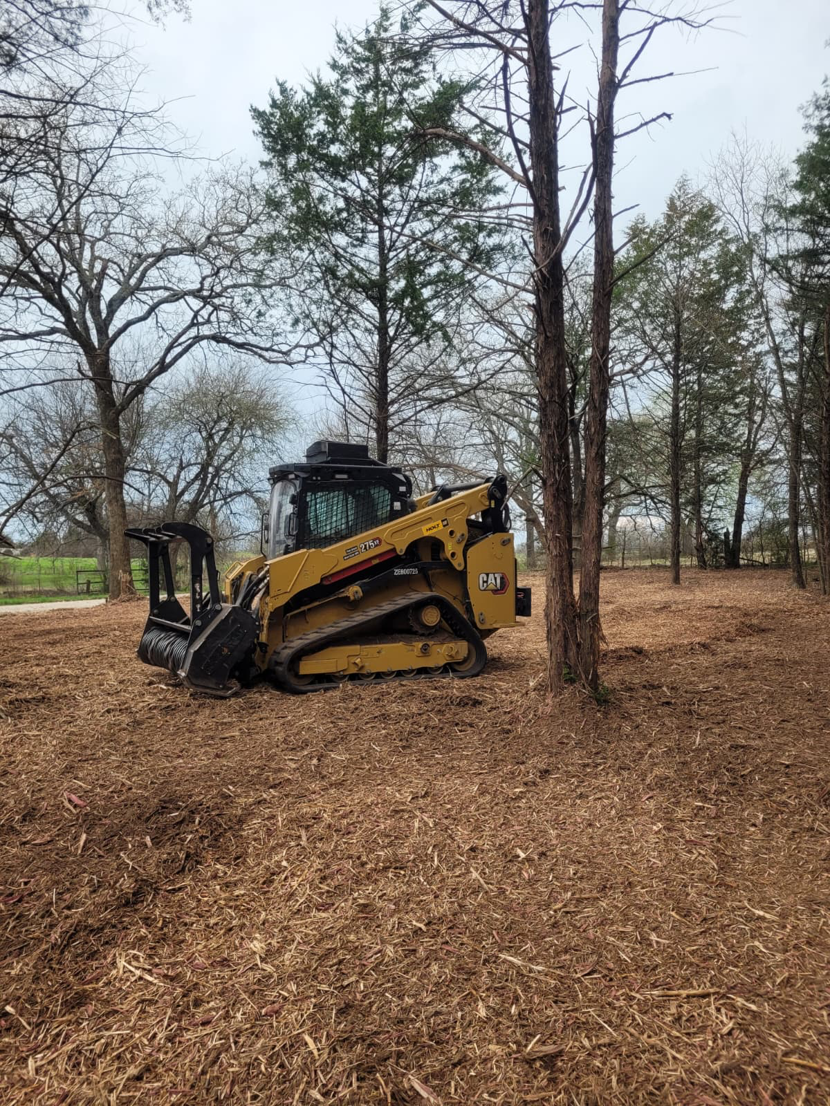 Orange bulldozer parked in a cleared field with trees in the background.