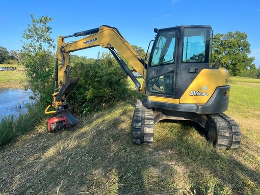 Orange bulldozer parked in a cleared field with trees in the background.