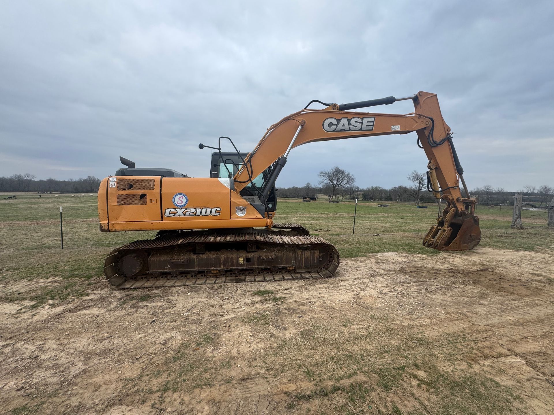 Orange bulldozer parked in a cleared field with trees in the background.