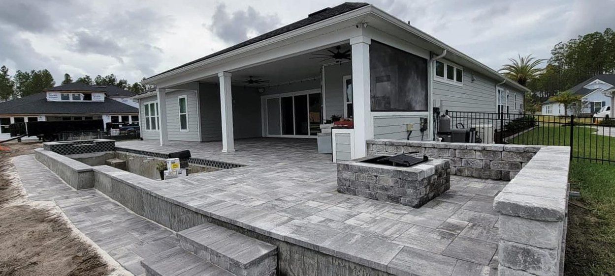 Backyard patio with gray paving stones, a fire pit, and a screened-in porch extending from a light gray house.
