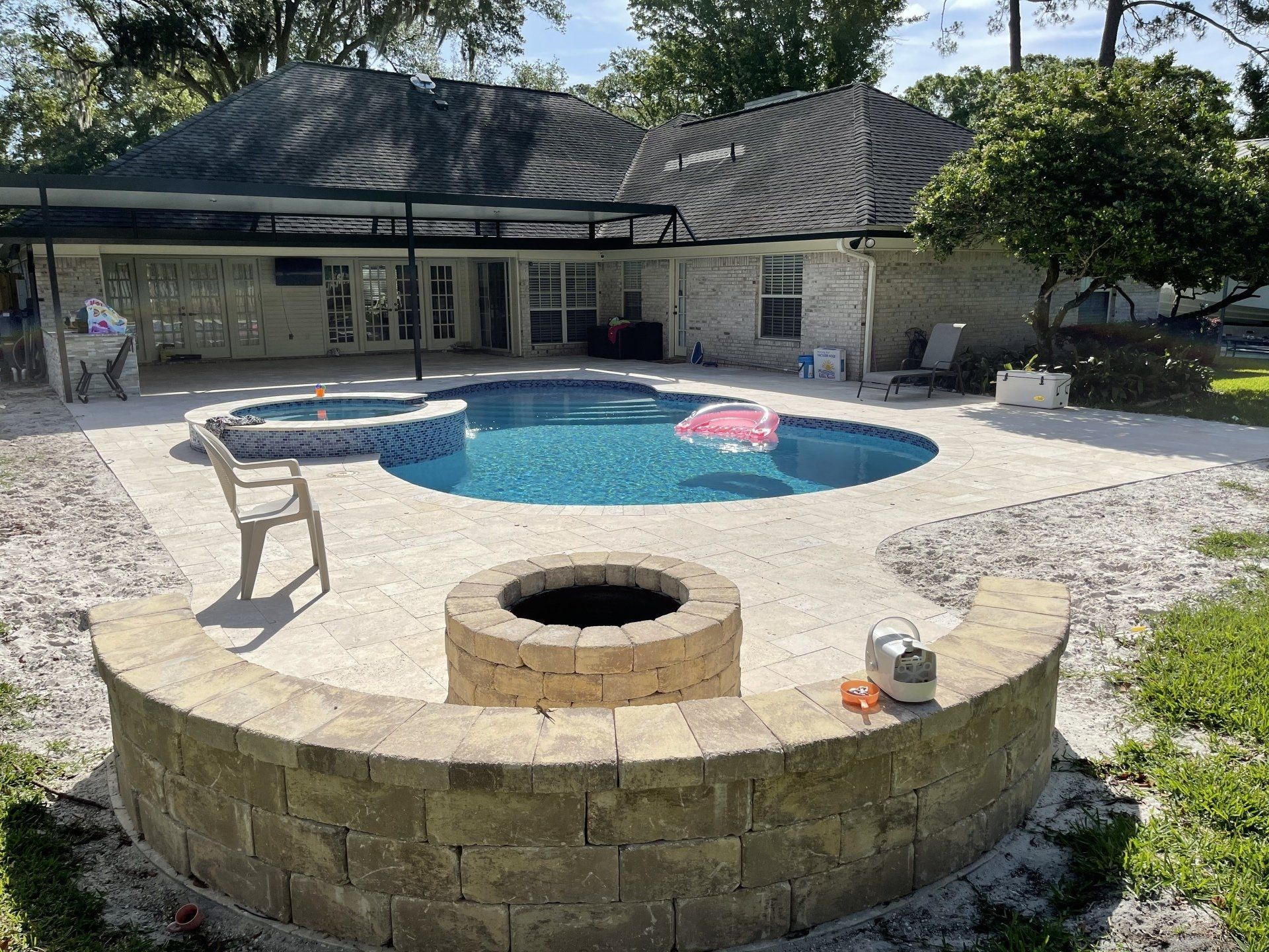A backyard with a pool, jacuzzi, and a fire pit. There's a house in the background.