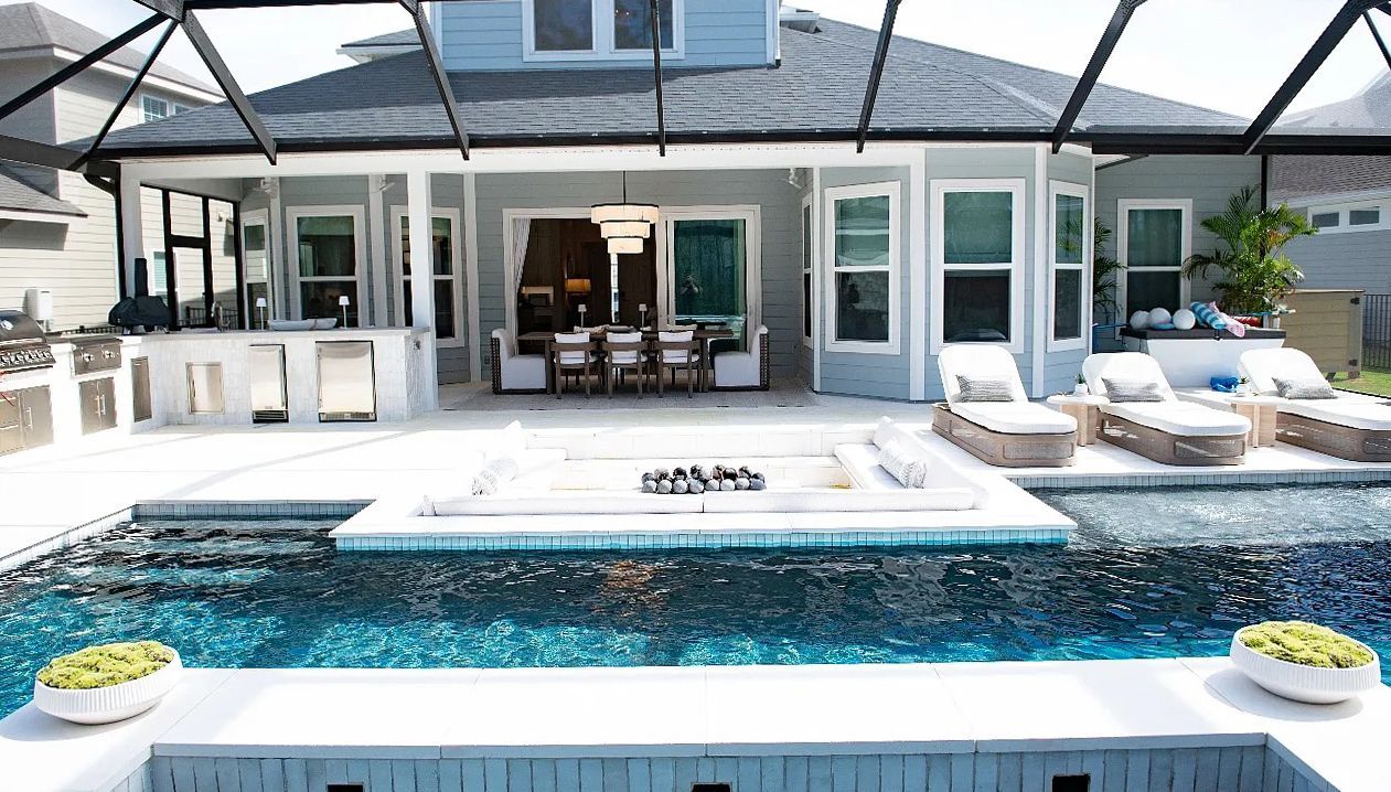 Backyard with a pool, outdoor kitchen, and covered patio. The pool has a fire pit and lounge chairs.