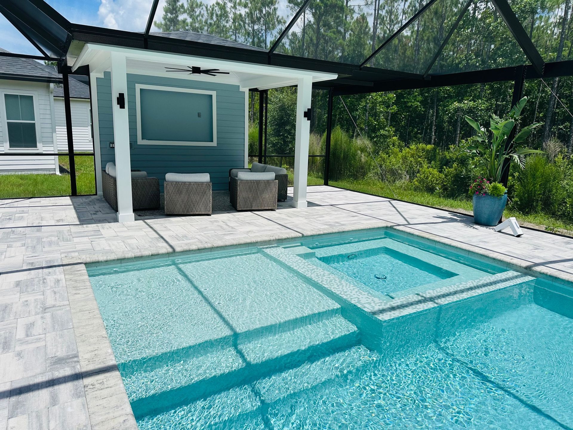 Swimming pool with a built-in spa, outdoor seating area, and lush greenery in the background.