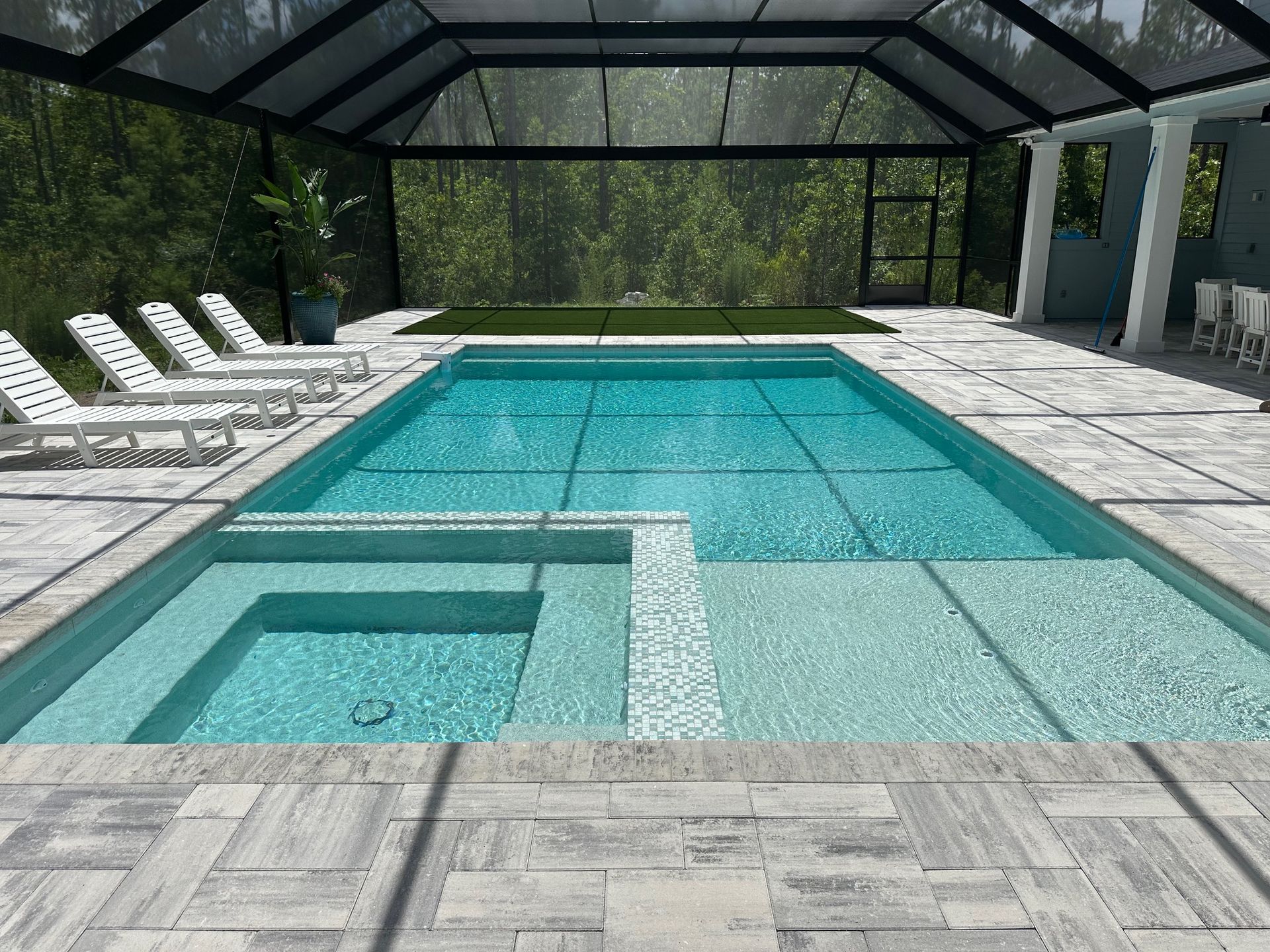 A rectangular swimming pool with a built-in jacuzzi. The pool area is enclosed in a screened structure, with chaise lounges and tiled decking.