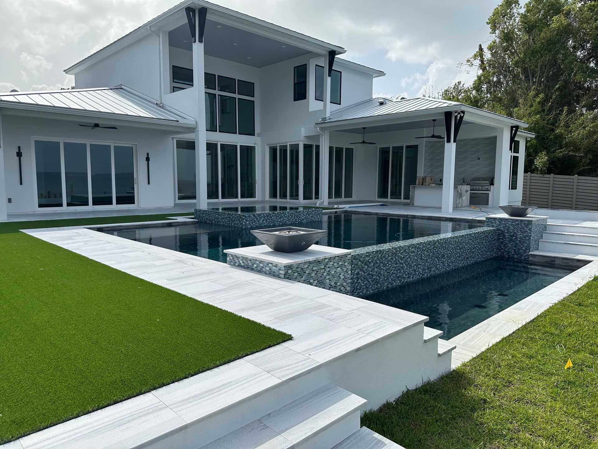 White modern home with a pool and green lawn. The pool has a dark surface and a tiled feature.