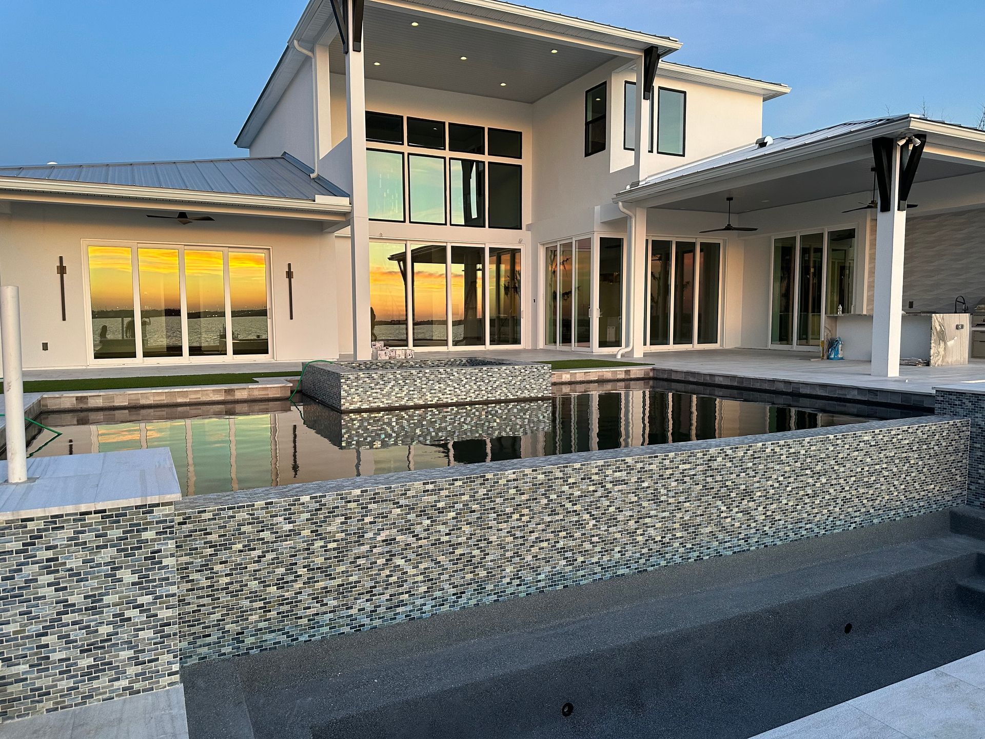 Modern white house with a pool reflecting a sunset. The pool has a textured mosaic border.