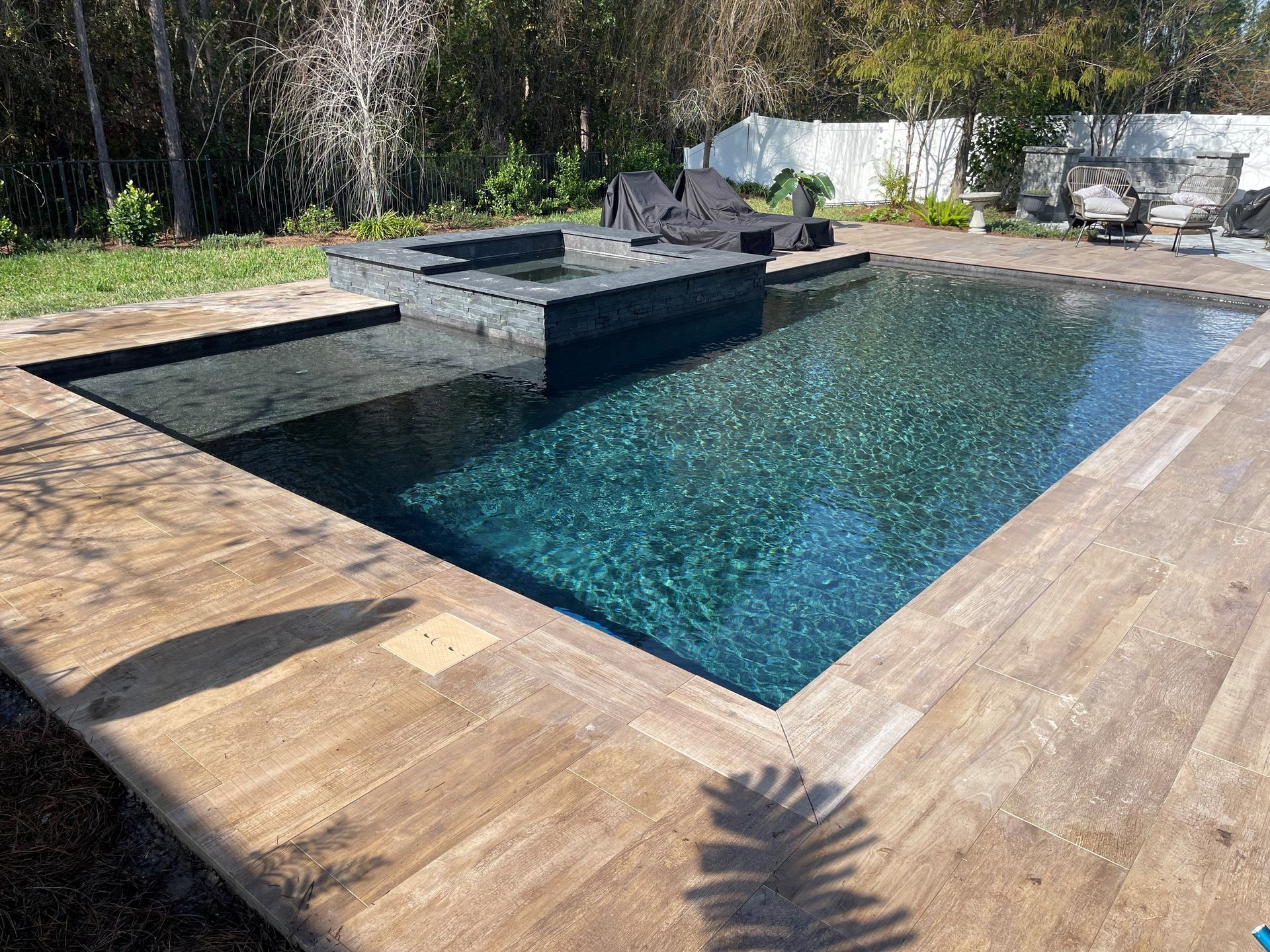 A modern backyard pool with dark tile and wooden decking, featuring a raised hot tub area.