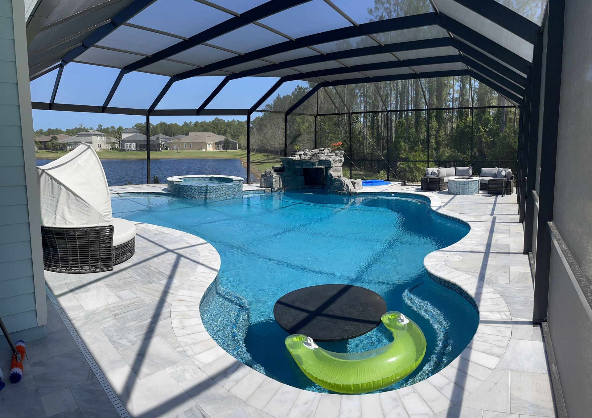 Pool and patio area with a blue pool, jacuzzi, and lounging furniture under a screened enclosure.