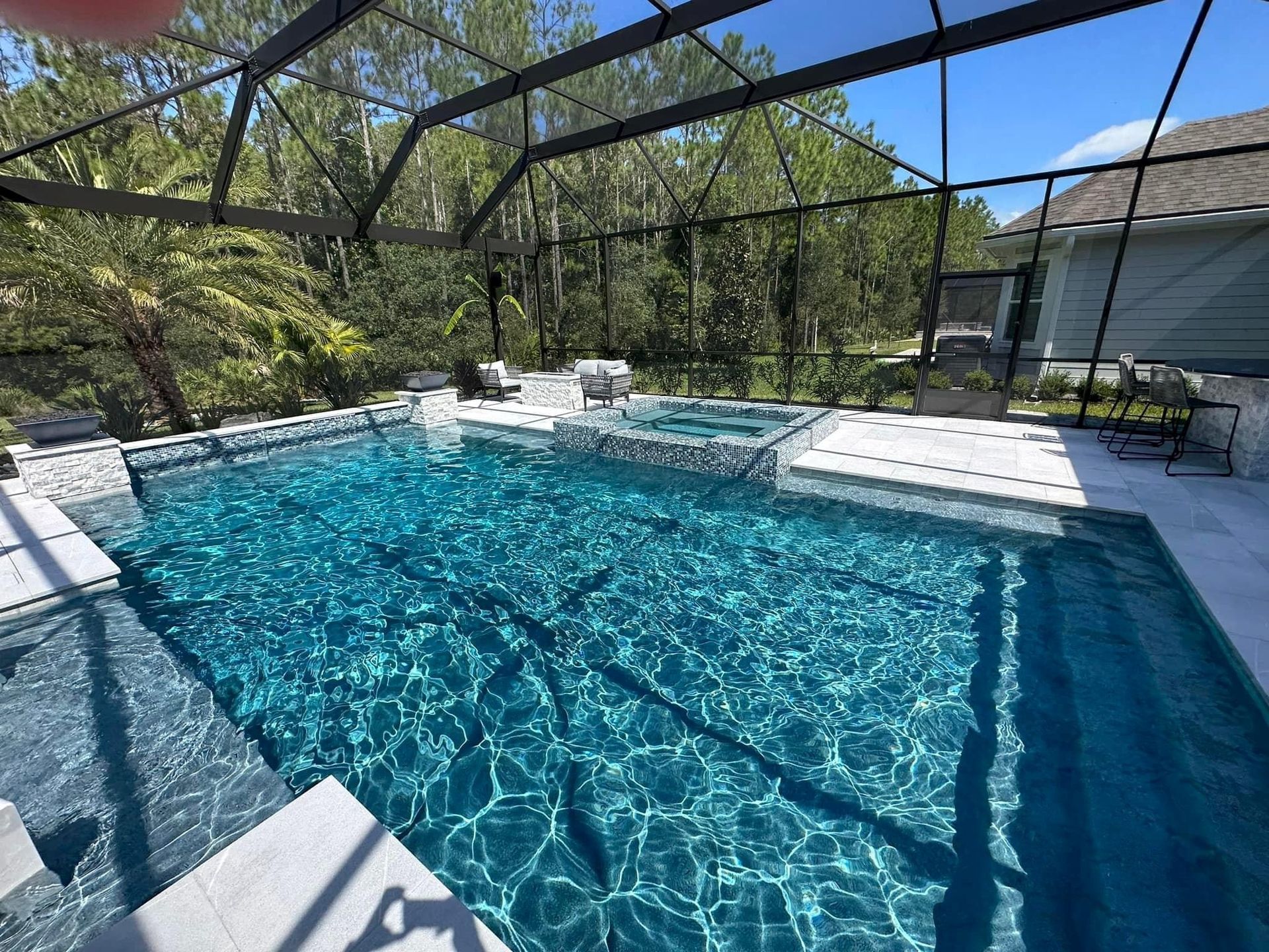 A rectangular swimming pool with turquoise water under a screened enclosure.  White tile surrounds the pool, with trees in the background.