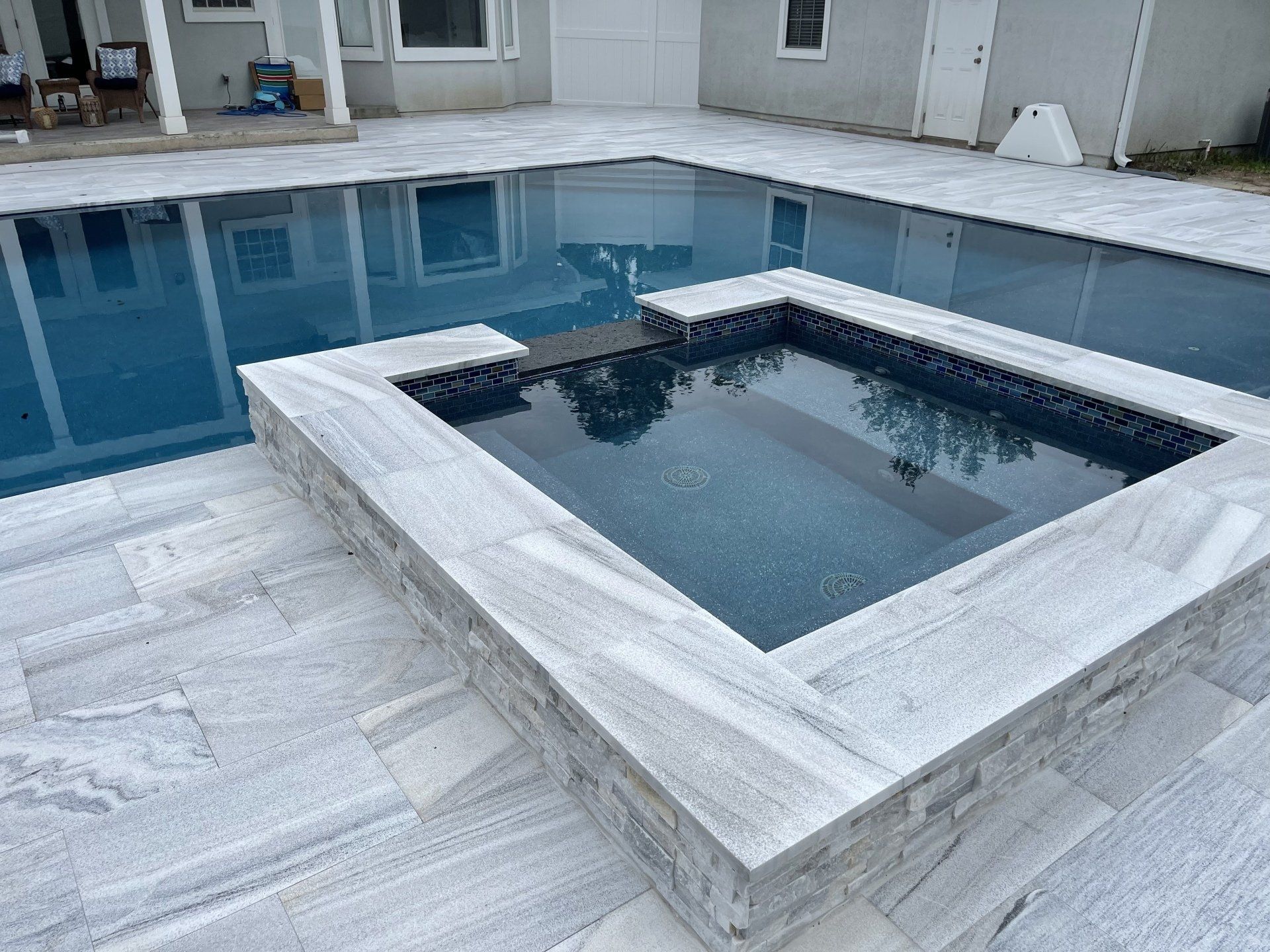 Pool with a built-in spa. Light gray stone surrounds the pool and spa, with blue water.