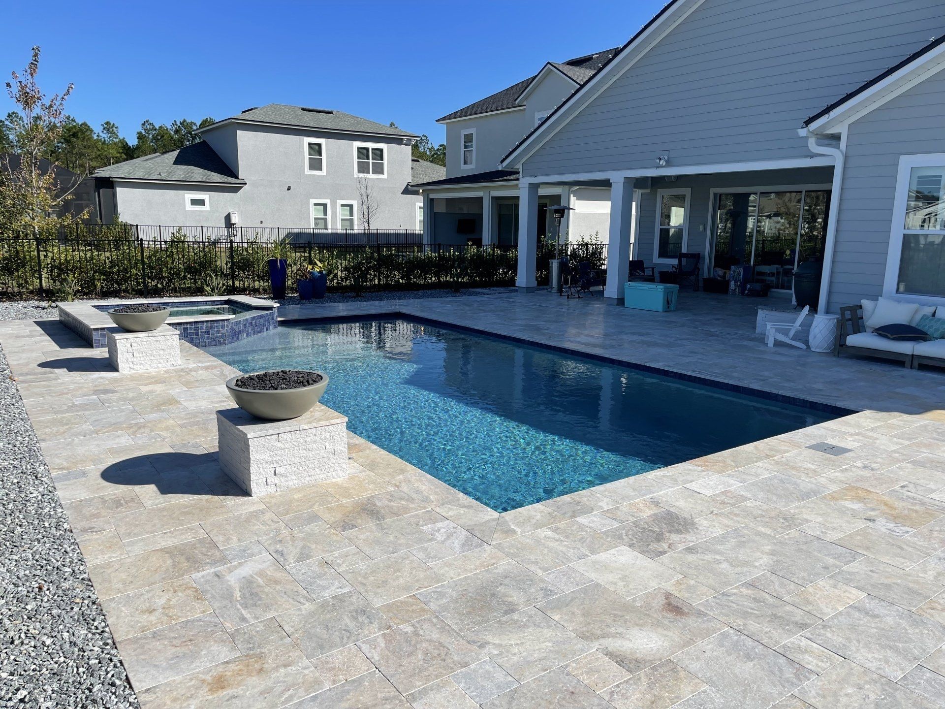 Backyard with a rectangular pool, stone patio, fire features, and a light gray house.
