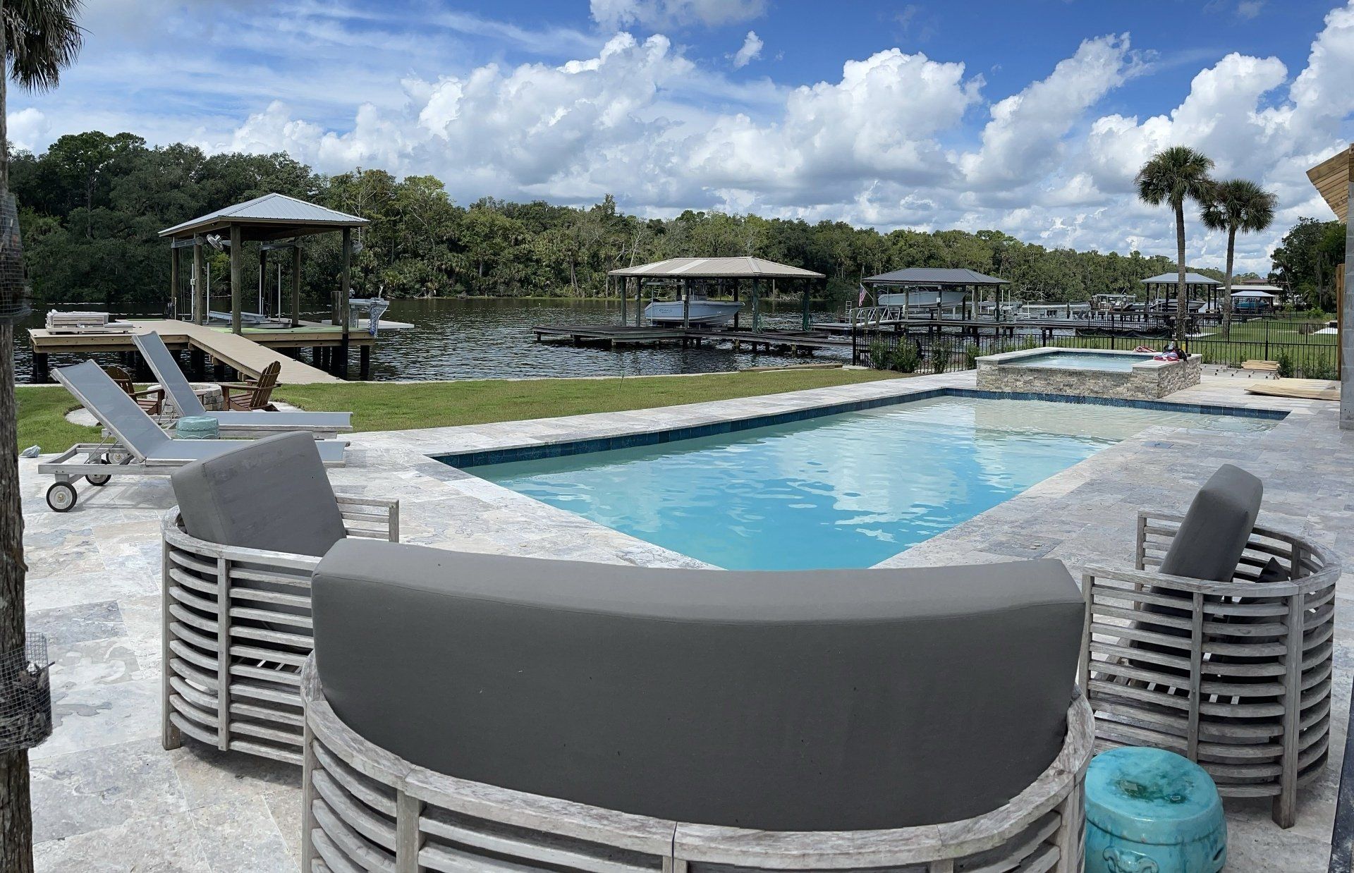 Backyard with a pool and seating area overlooking a body of water with docks and lush greenery under a cloudy sky.