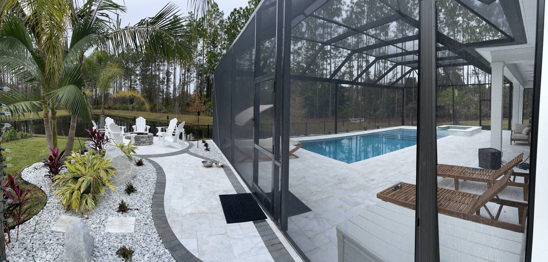 A screened-in pool area with a white stone patio. There's a pool, lounge chairs, and landscaping with white stones and plants.