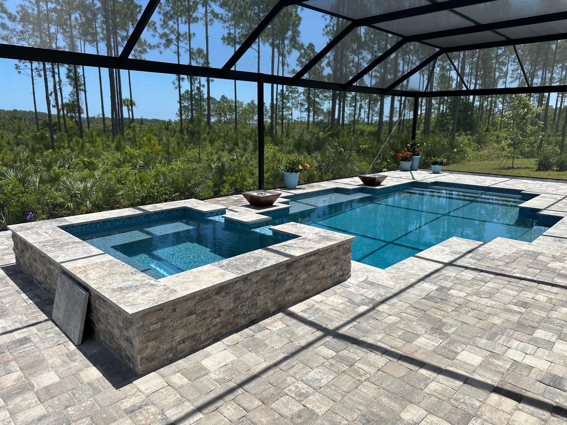 Pool with jacuzzi, screened enclosure, and paver patio. The pool and jacuzzi have blue tiles, while the enclosure is black.