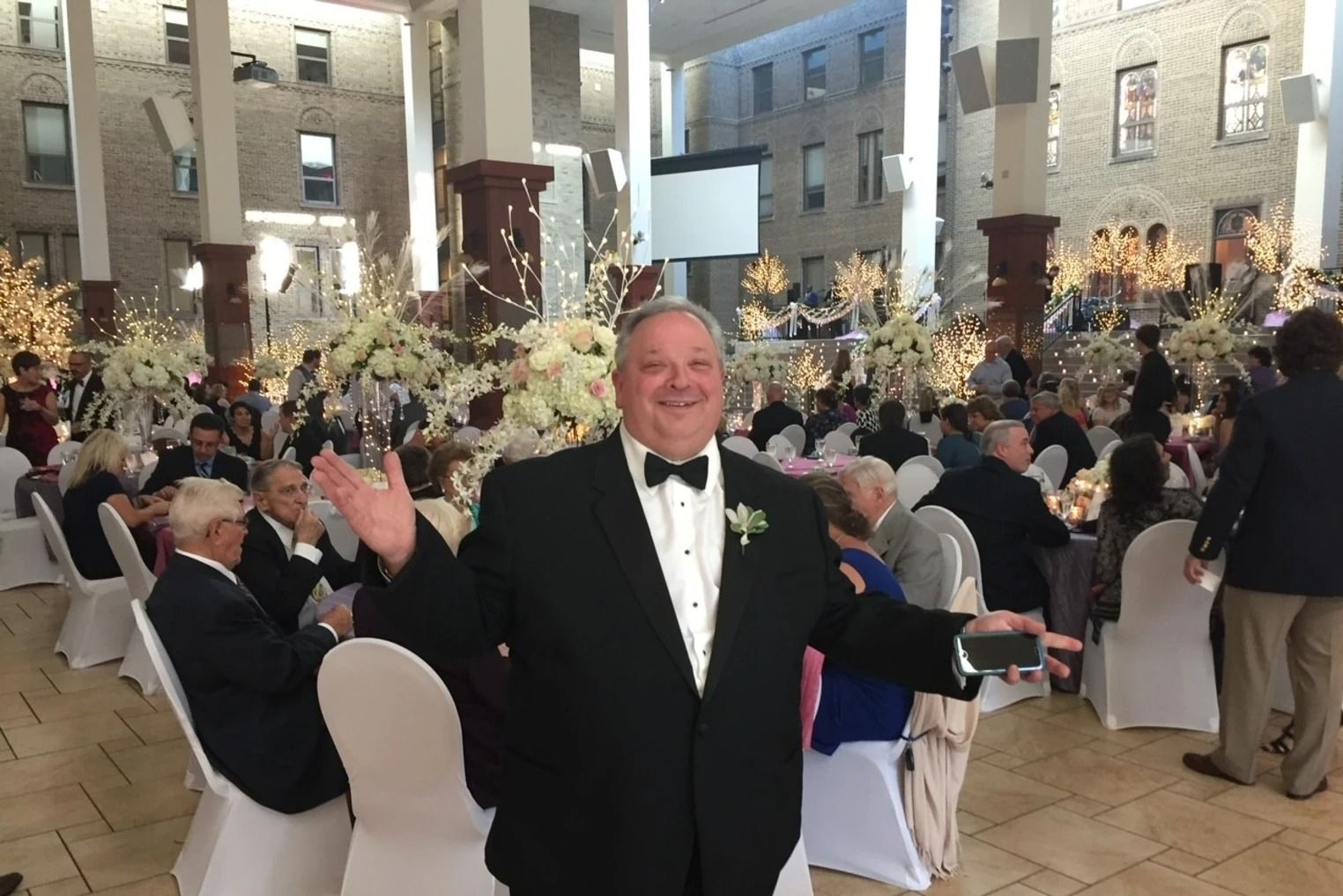 A man in a tuxedo is standing in front of a crowd of people at a wedding reception